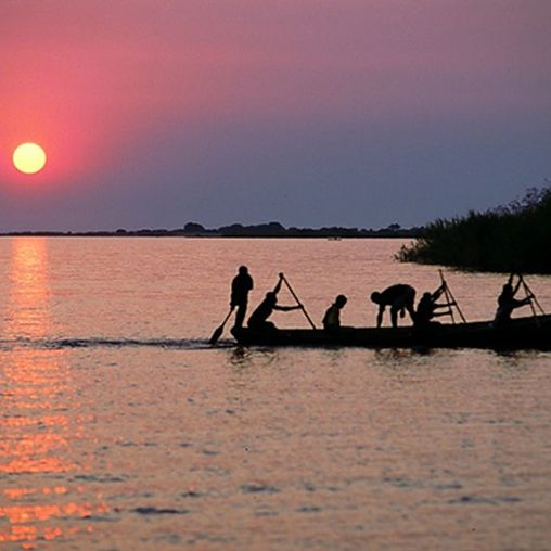 Menschen auf länglichem Boot paddeln auf Wasser im Sonnenuntergang