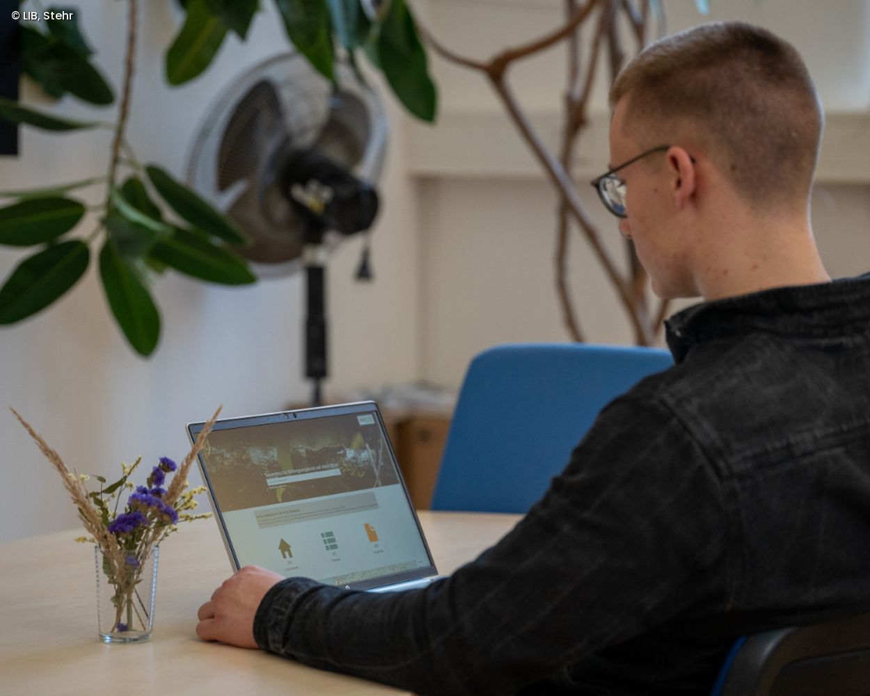Mann sitzt an einem Tisch und schaut auf einen Laptop-Bildschirm.