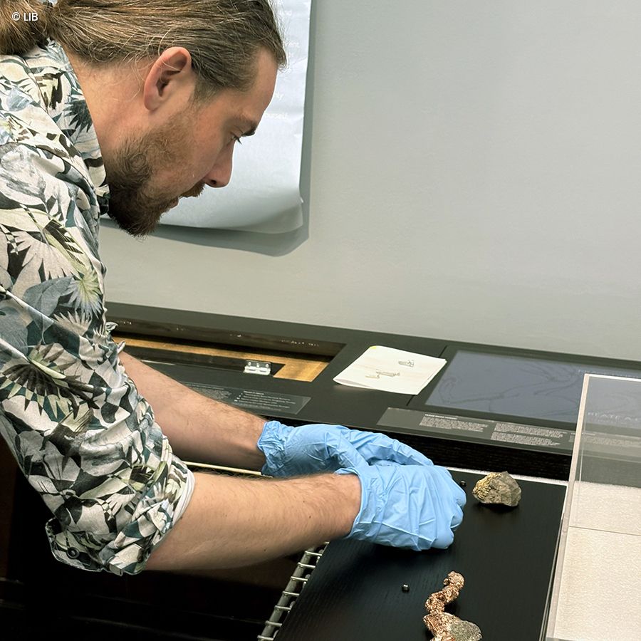 Person wearing blue gloves placing two rock samples on a black display surface in a museum or exhibition.