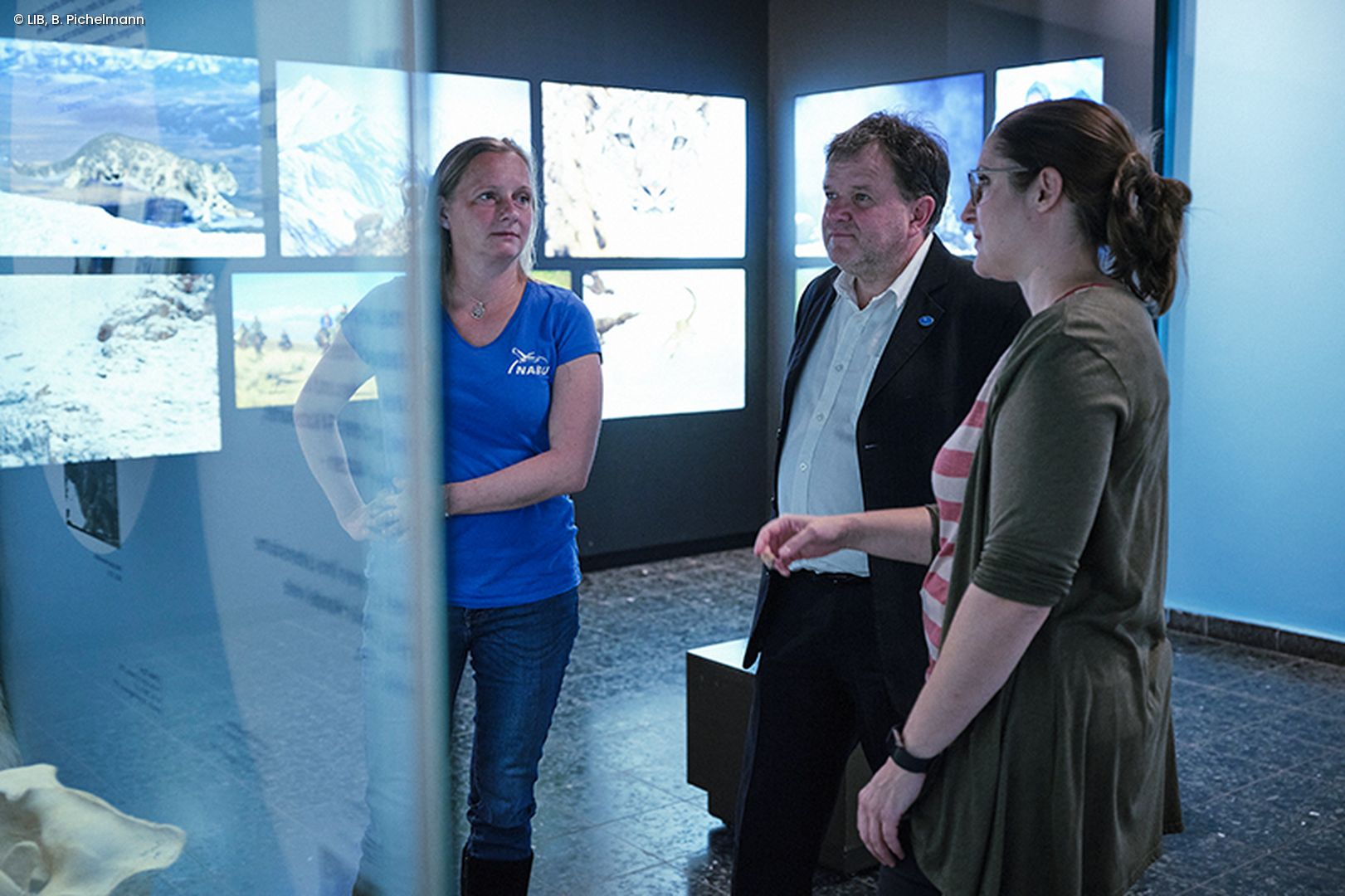 3 Menschen im Gespräch vor Ausstellungsvitrine