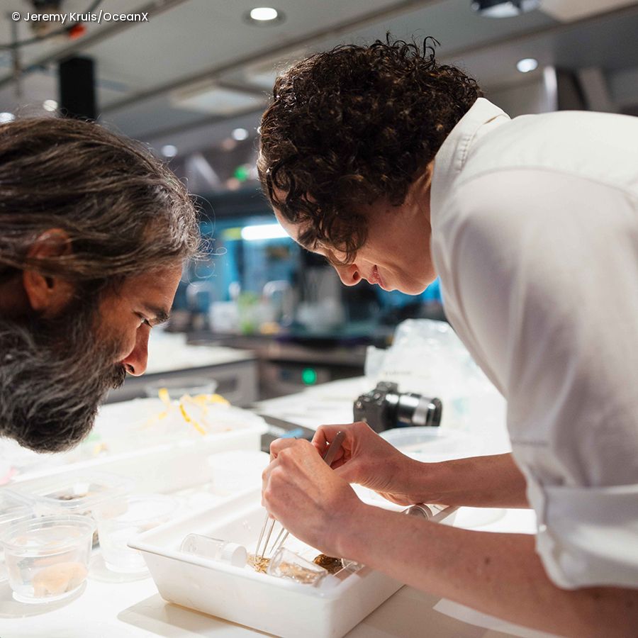 Two people leaning over a table with lab equipment and a camera in the background