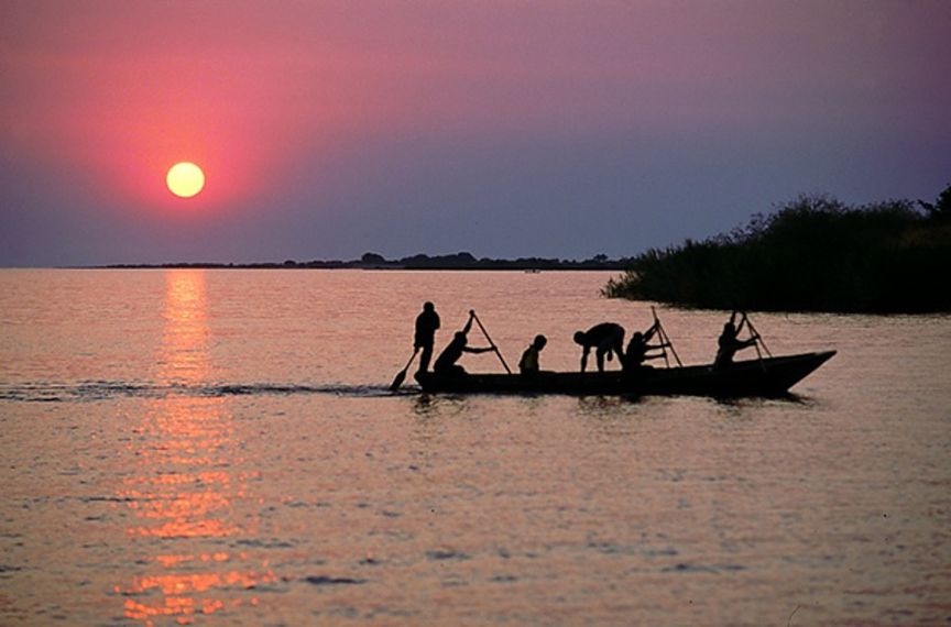 Menschen auf länglichem Boot paddeln auf Wasser im Sonnenuntergang