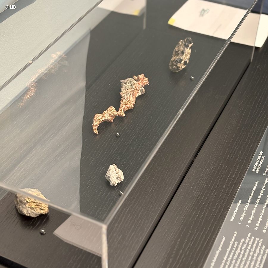 Display case with several irregularly shaped silver and copper ore samples on a dark surface under glass cover